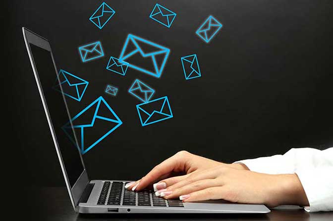 Hands typing on a silver laptop with blue email icons flying out of the screen